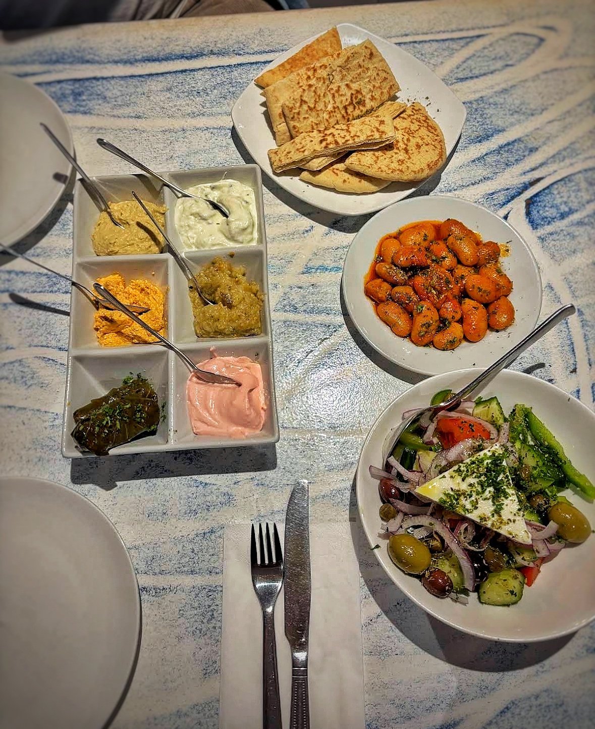 Round one of Zorba's meze laid out — hummus and dips, pitta bread, roasted vegetables and fresh salad on a blue patterned tablecloth